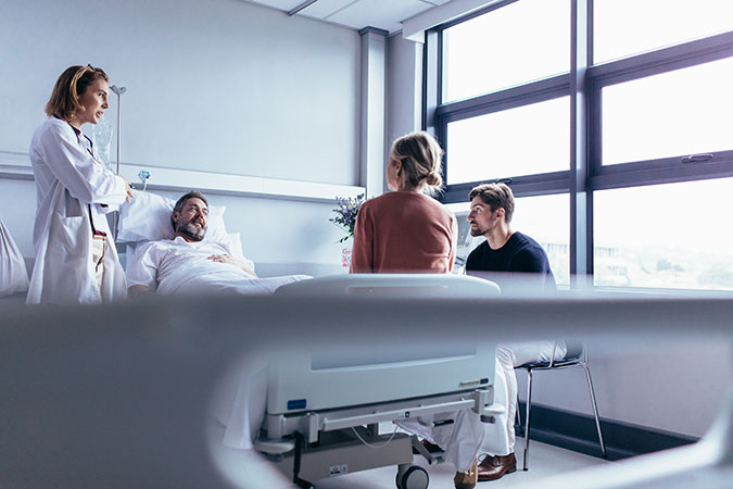female doctor at man's bedside in hospital talking to his family