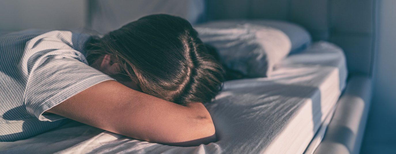 person lying on their front on a bed with arm over their face
