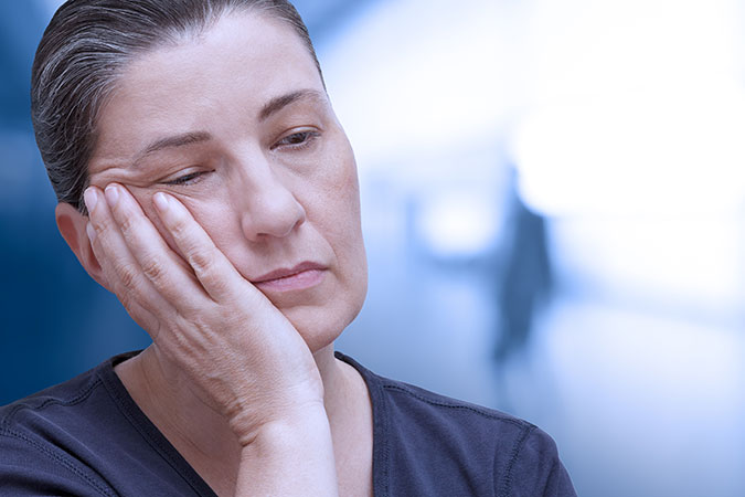 woman with hand on cheek holding her head up looking tired
