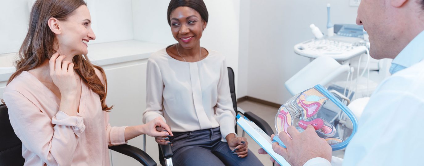 two women looking at each other holding hands and smiling whilst a medical professional talks to them