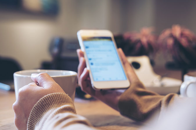 arms of a person holding a mug and looking at messages on their phone