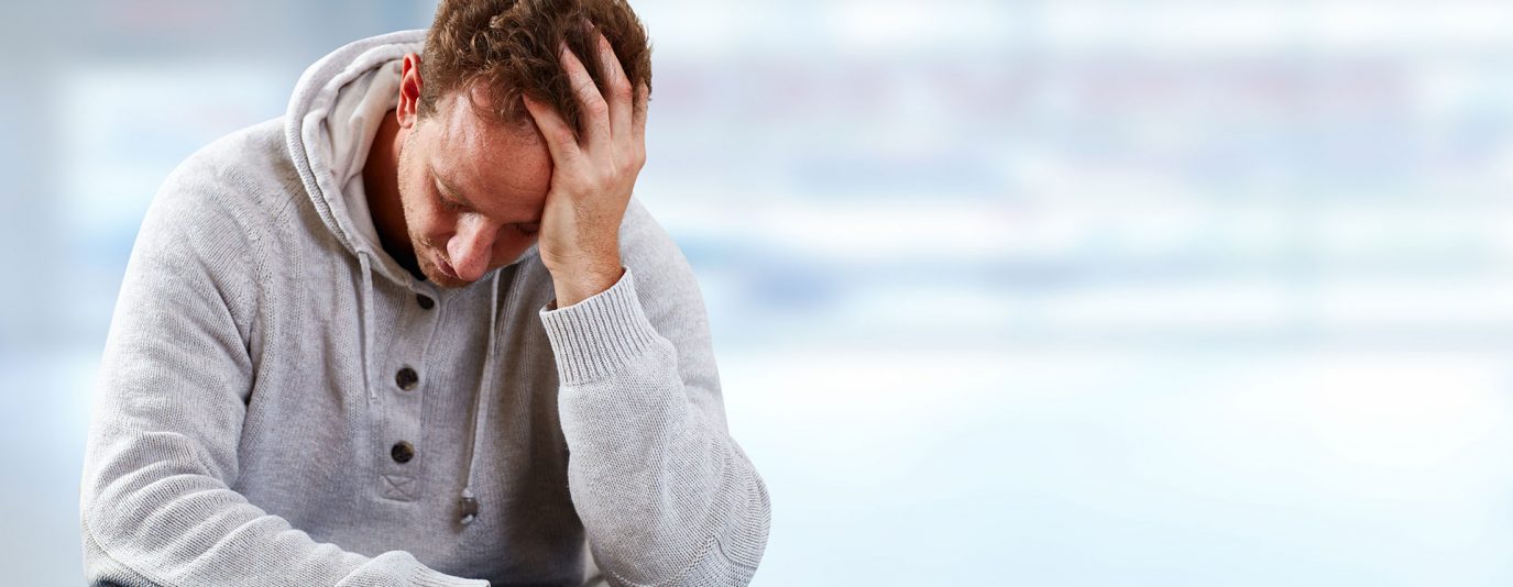 man in grey jumper sat with hand on head looking down