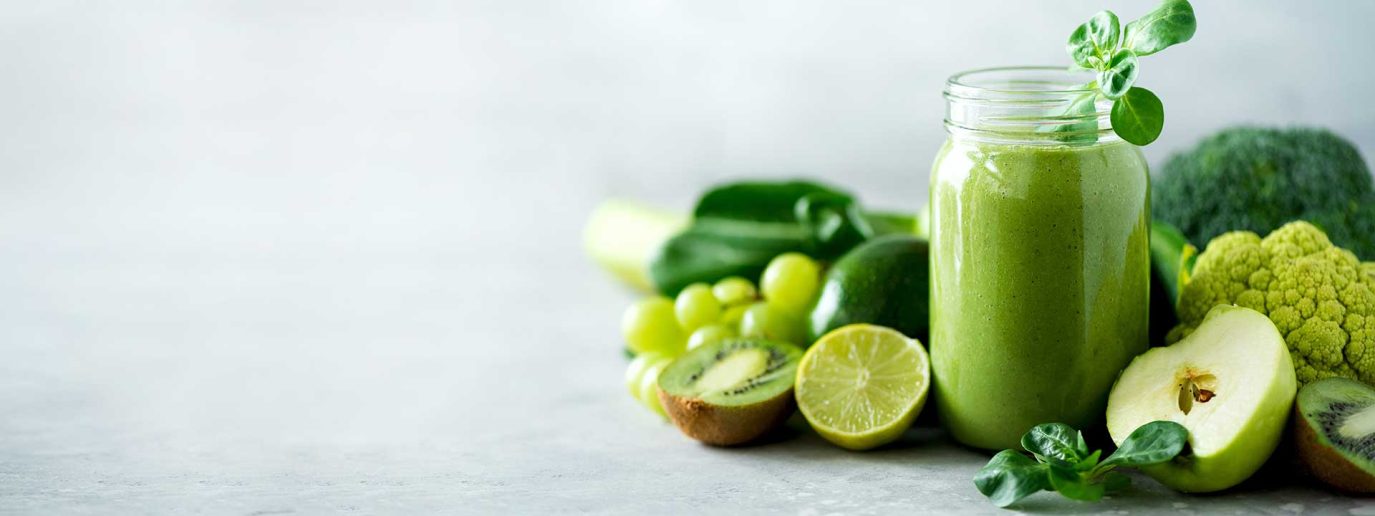 Green smoothie with ingredients around the outside of the jar including kiwi, grapes, apple and broccoli